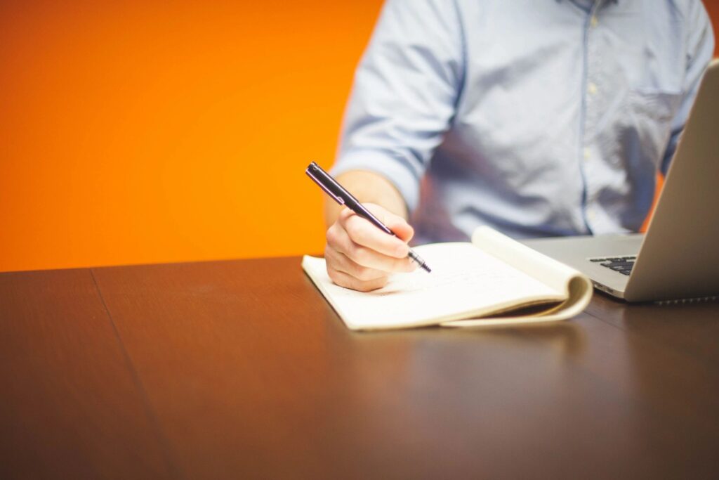 Man writing with an orange wall behind him