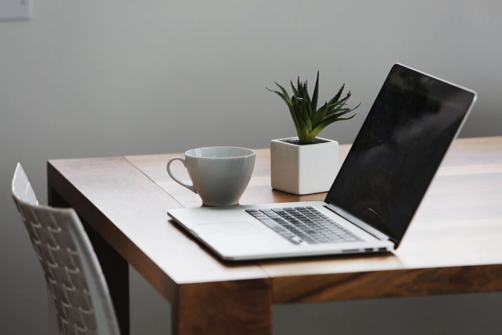 Laptop on a desk with a coffee cup and a plant